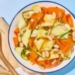 Zucchini ribbon salad in a bowl next to a cloth napkin and wooden serving utensils.