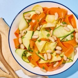 Zucchini ribbon salad in a bowl next to a cloth napkin and wooden serving utensils.