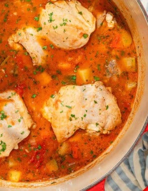 Chicken stew in a large pot next to a stack of 2 bowls with 2 spoons.