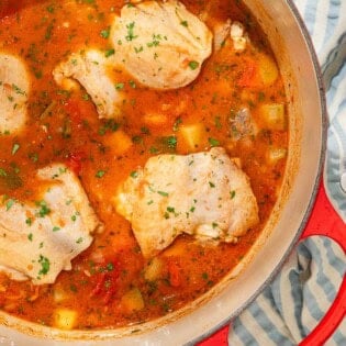 Chicken stew in a large pot next to a stack of 2 bowls with 2 spoons.