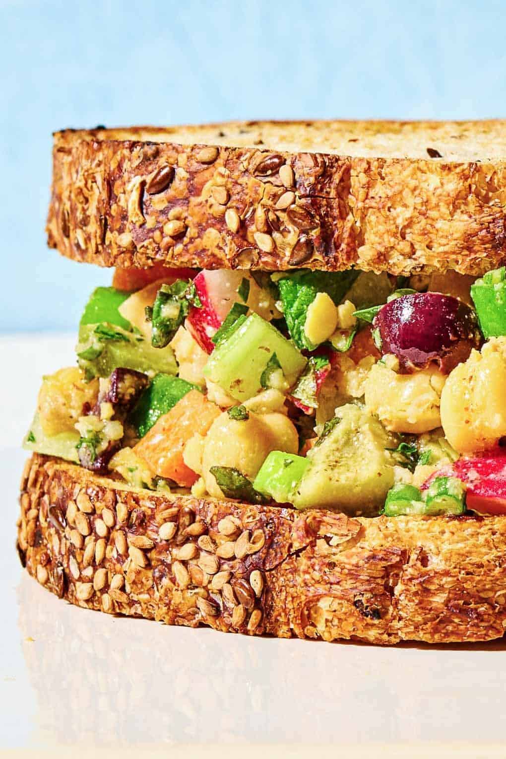 Close up of chickpea salad sandwich, showing the layers of fresh veggies, olives and more.