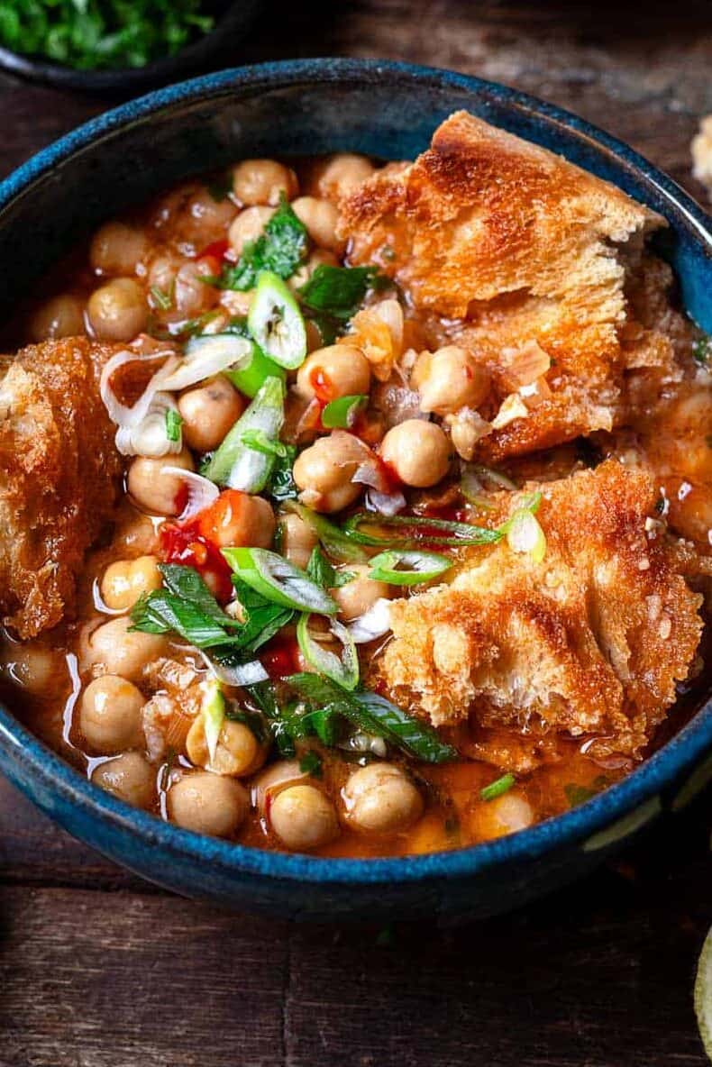 lablabi tunisian chickpea stew in a bowl, next to bowls of various toppings.