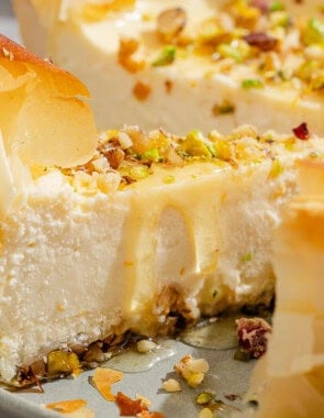 A close up of a slice of baklava cheesecake on a platter with the rest of the cake.