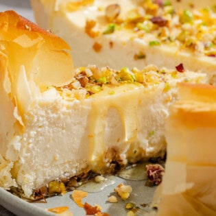 A close up of a slice of baklava cheesecake on a platter with the rest of the cake.