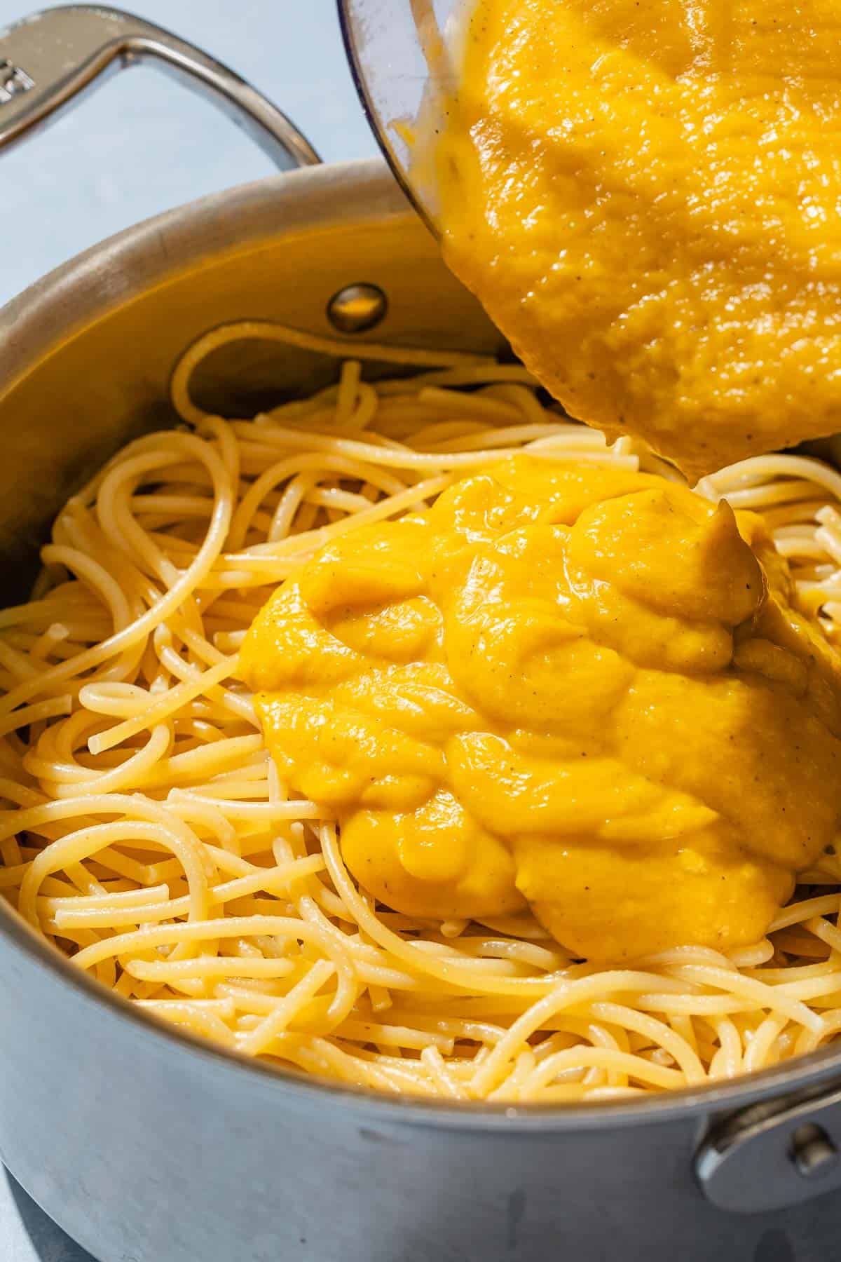 Butternut squash pasta sauce being poured over cooked spaghetti in a pot.