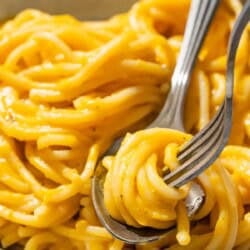 Butternut squash pasta sauce mixed with spaghetti in a bowl with a fork and a spoon.