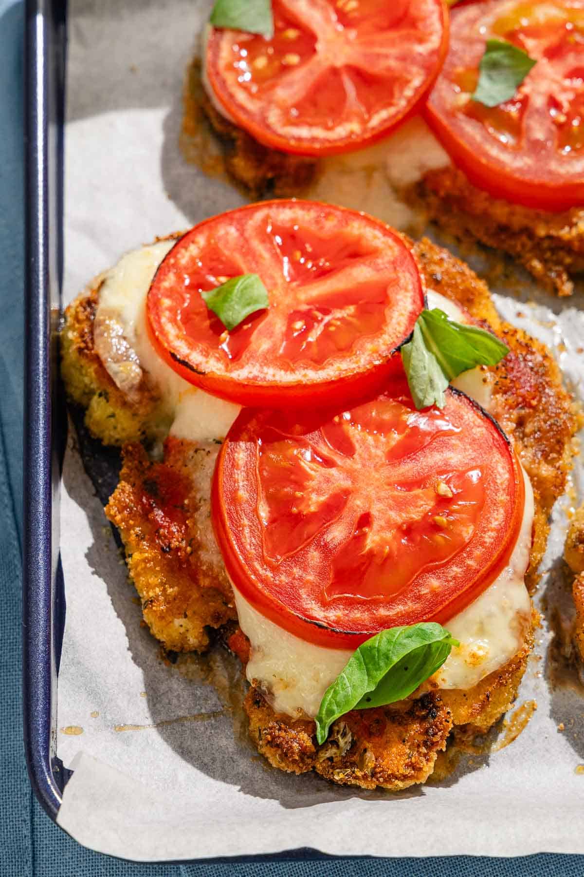 A close up of a piece of baked cauliflower parmesan on a parchment lined sheet pan.