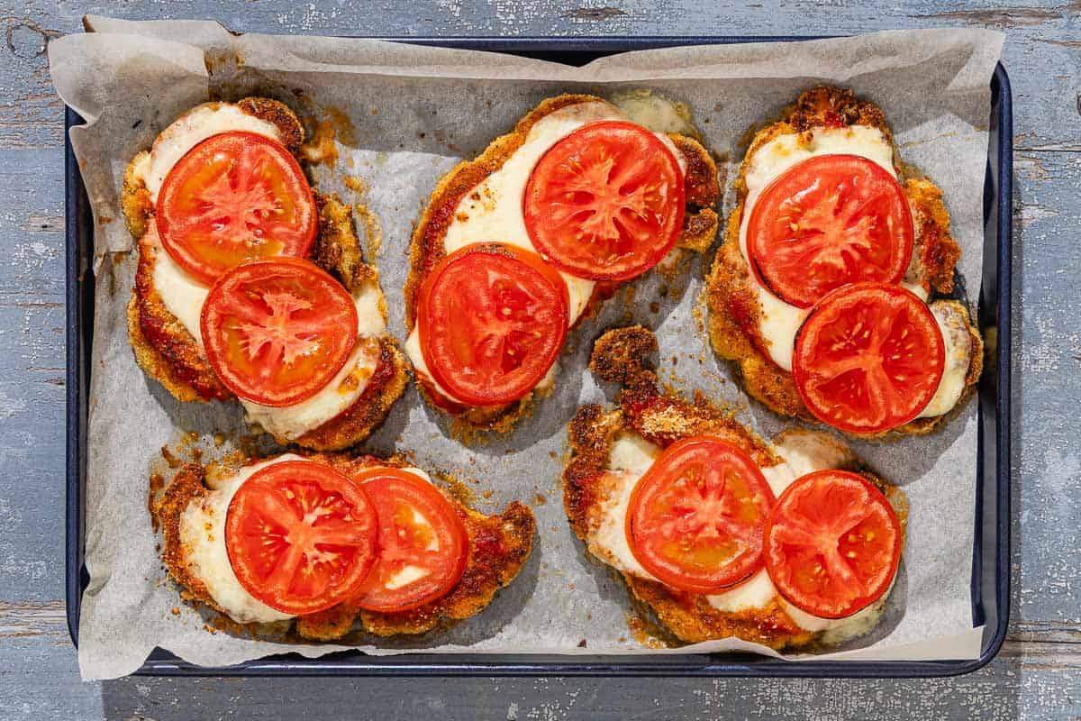 Five pieces of baked cauliflower parmesan on a parchment lined sheet pan.