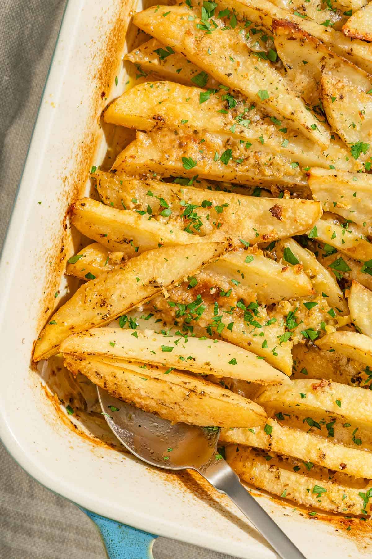 A close up of the greek potatoes in a baking dish with a serving spoon.