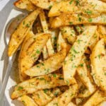 Greek lemon potatoes on a platter with a serving spoon next to a bowl of chopped parsley.