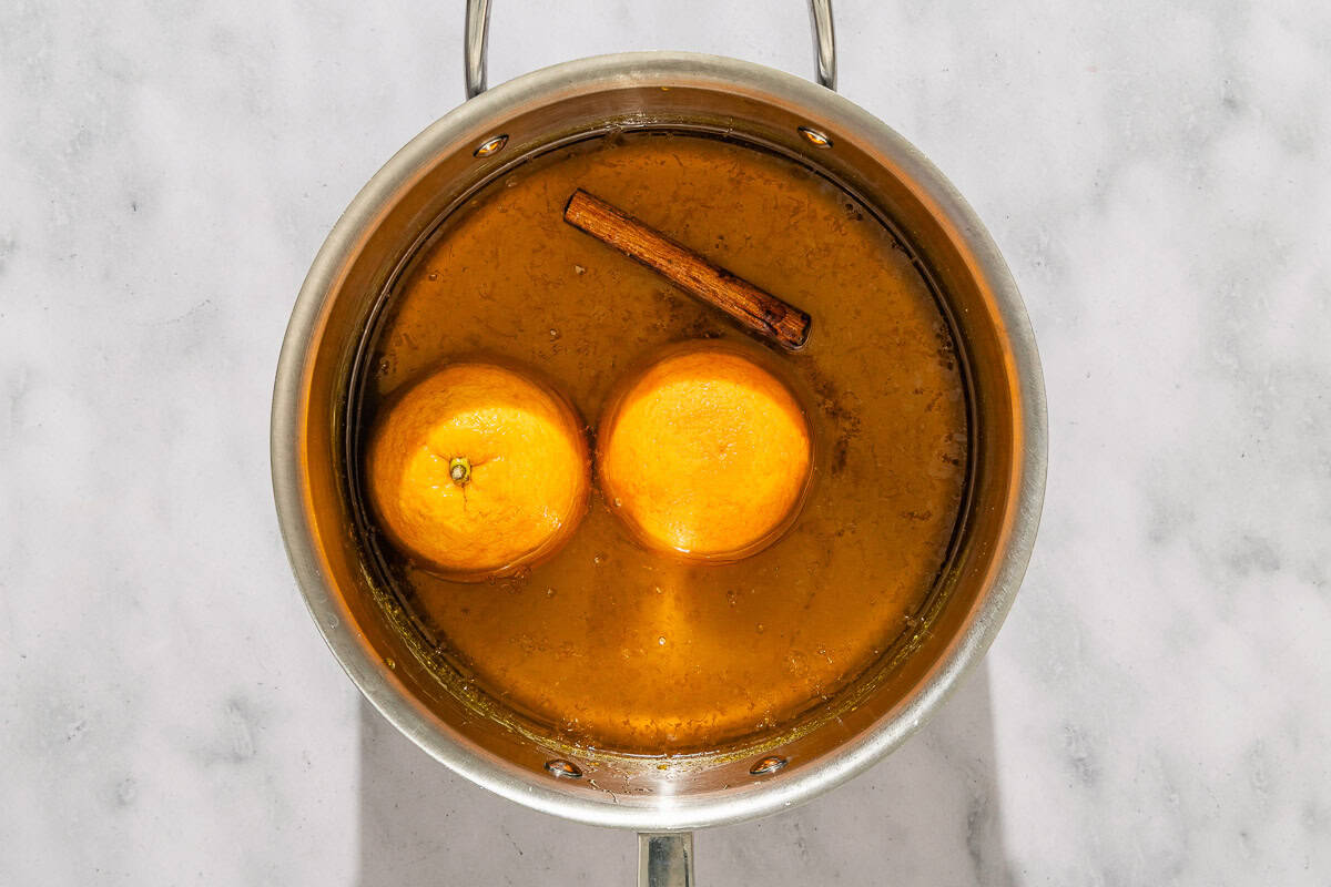 The syrup for the melomakarona in a pot with 2 whole oranges and a cinnamon stick.
