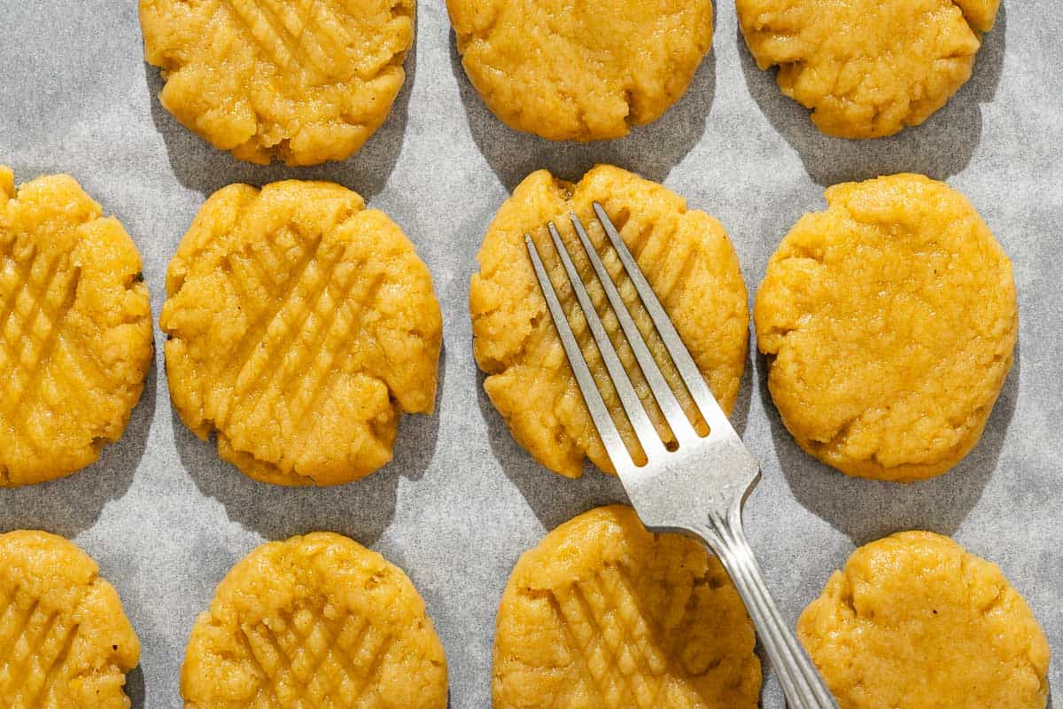 An overhead photo of the signature pattern for melomakarona being pressed into a cookie with a fork. Surrounding this are several other unbaked melomakarona.
