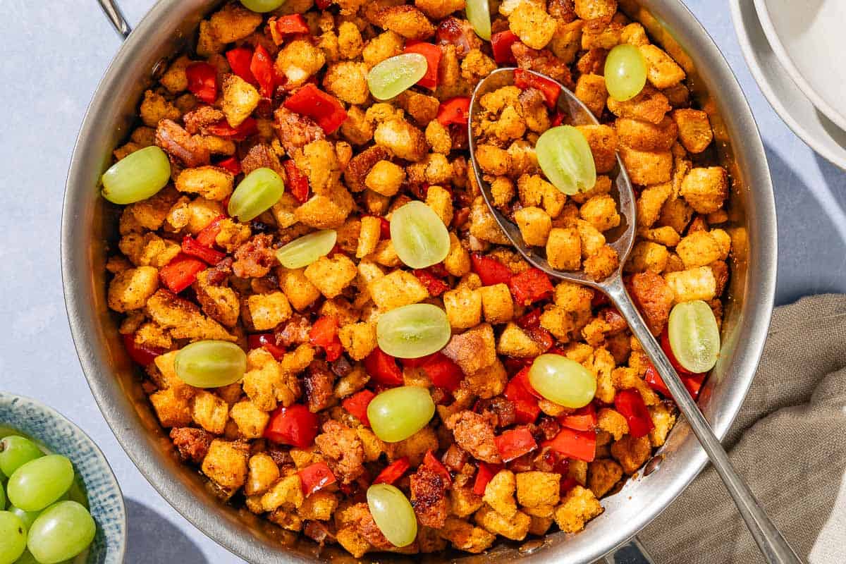 Migas in a tall sided skillet with a serving spoon next to a stack of small bowls and a bowl of grapes.
