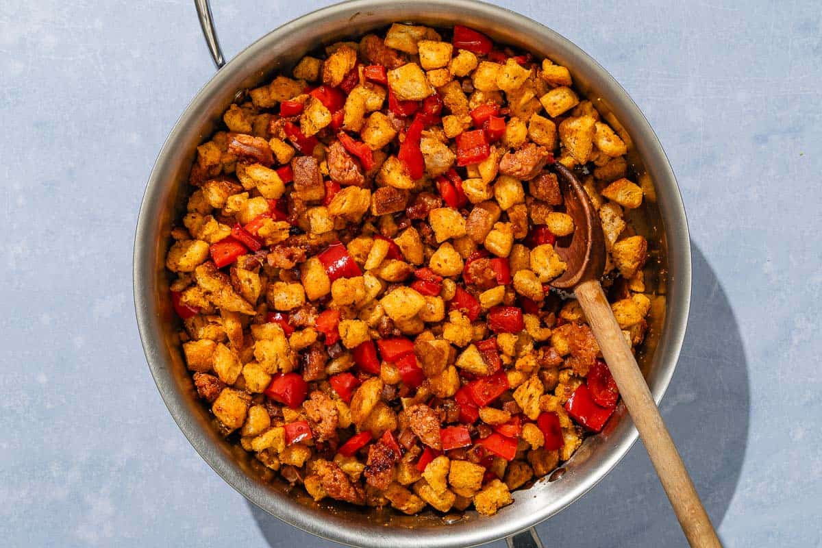 The migasbeing cooked in a tall sided skillet with a wooden spoon.