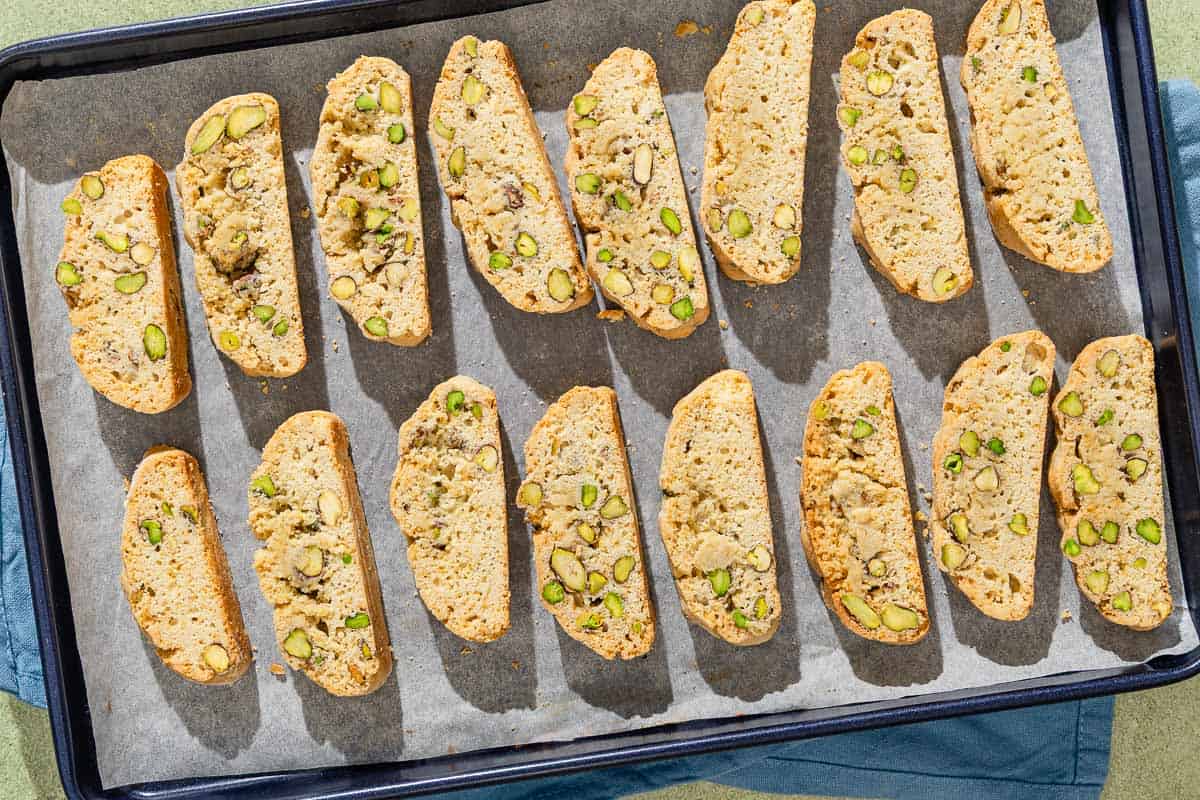 An overhead photo of several slices of pistachio biscotti on a parchment lined sheet pan.