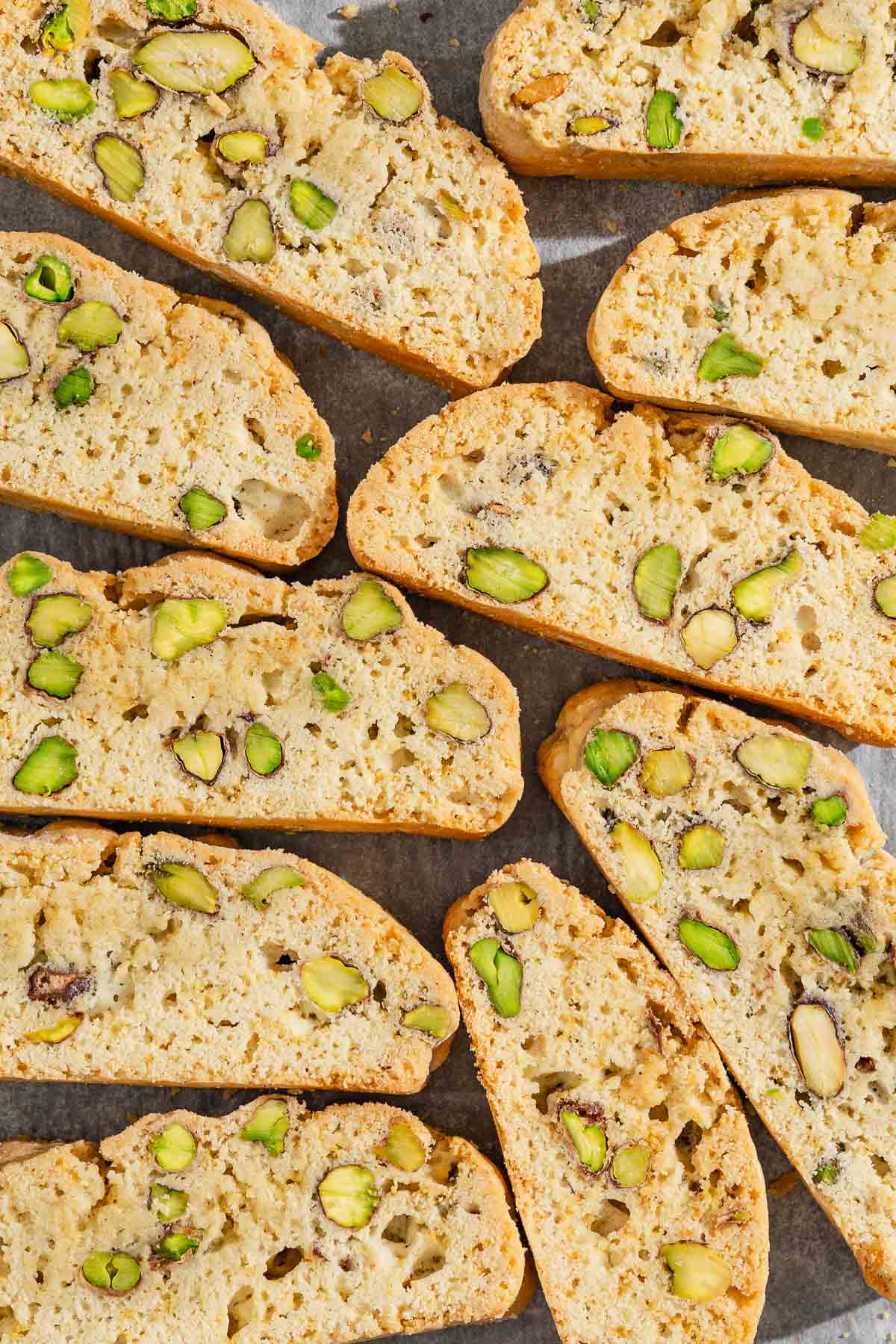 A close up of several slices of pistachio biscotti on a parchment lined sheet pan.