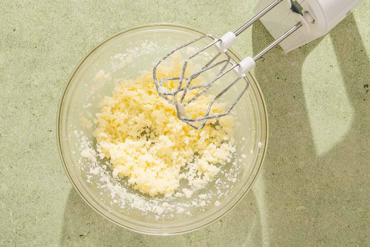 The butter and sugar for the baklava cheesecake mixed together in a bowl next to a hand mixture.