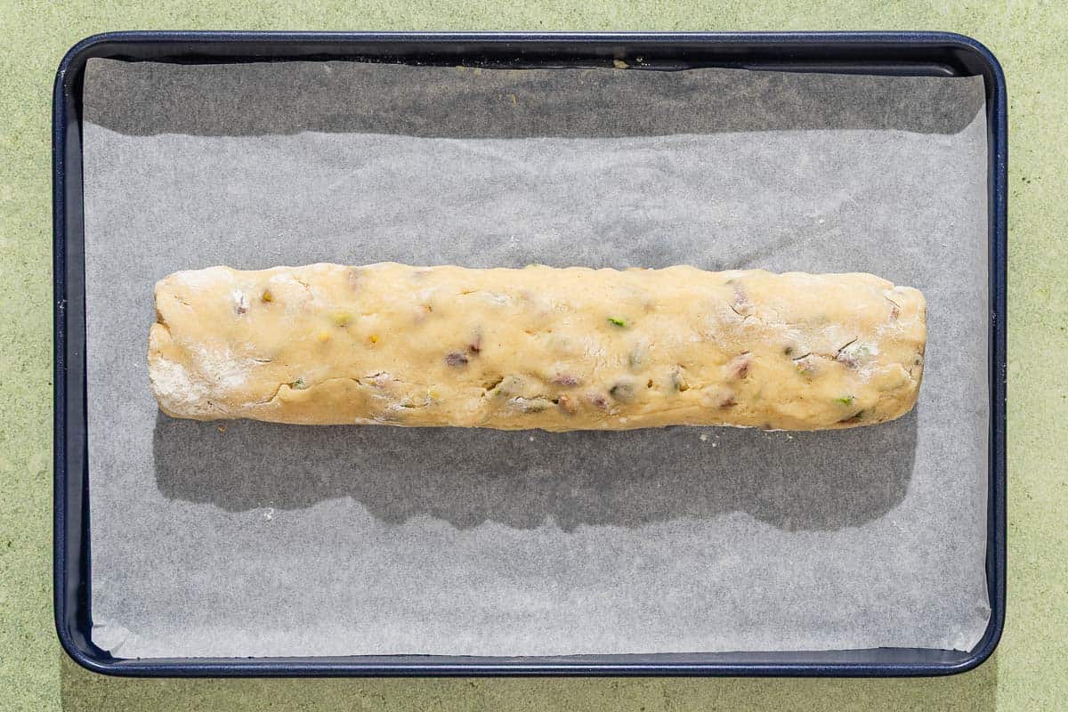 The dough for the pistachio biscotti rolled into a log on a parchment lined sheet pan.