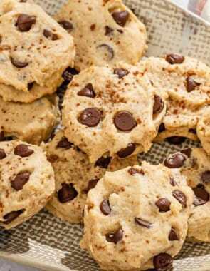 Several tahini chocolate chip cookies on a platter next to a kitchen towel.