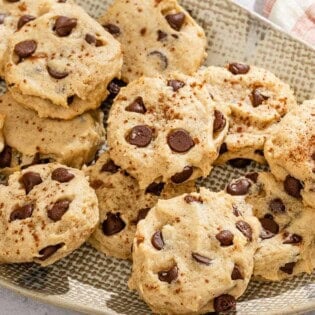 Several tahini chocolate chip cookies on a platter next to a kitchen towel.