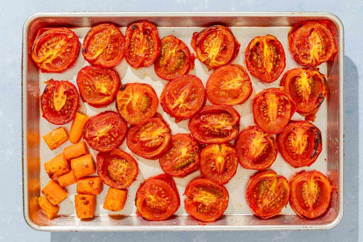 Roasted halved roma tomatoes and carrot pieces on a sheet pan.