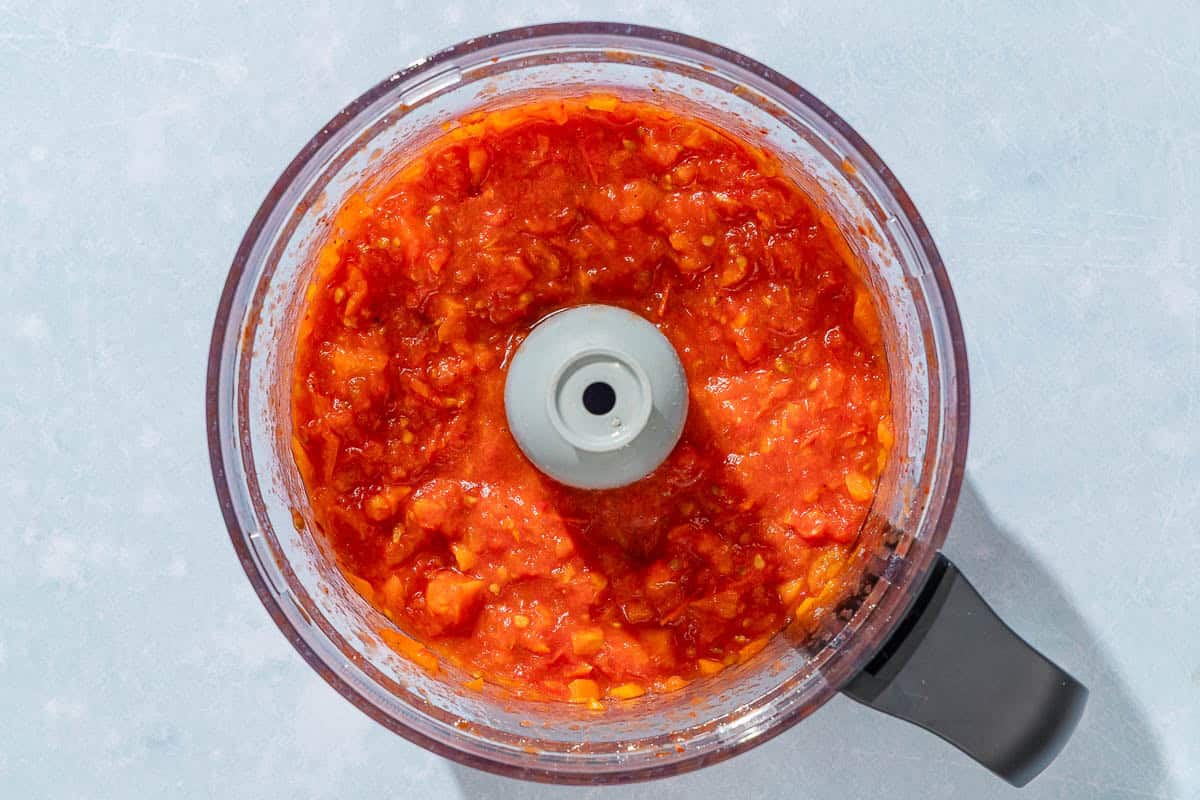 The blended roasted tomatoes and carrots in the bowl of a food processor.