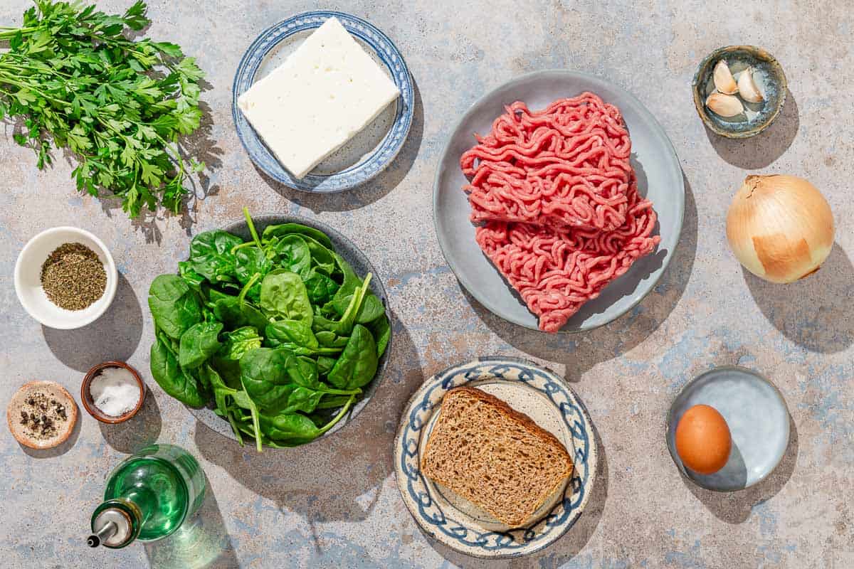 Ingredients for turkey meatballs including ground turkey baby spinach, whole wheat bread, onion, garlic, feta cheese, egg, parsley, dried mint, olive oil, salt and black pepper.