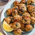 Several turkey meatballs on a platter with a serving spoon and lemon wedges. Next to this is a bowl of chopped parsley.