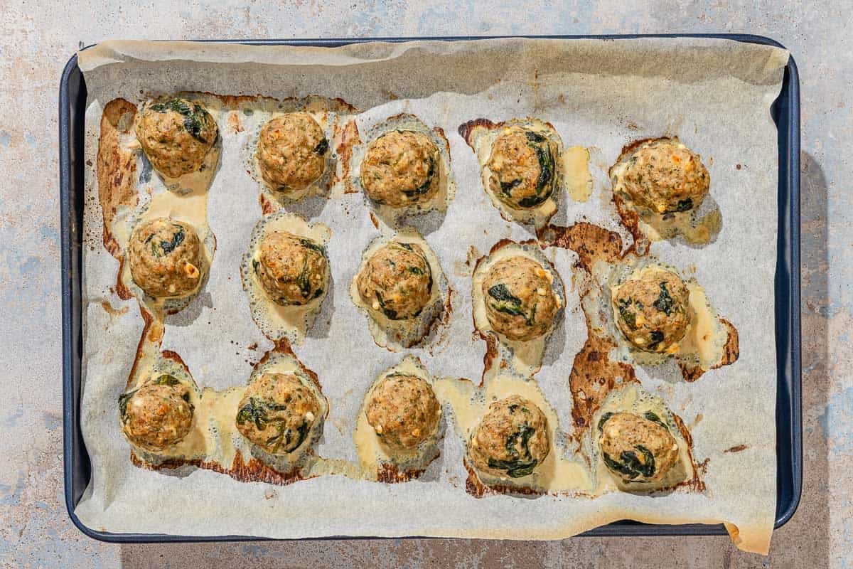 Several baked turkey meatballs spread evenly on a parchment lined sheet pan.