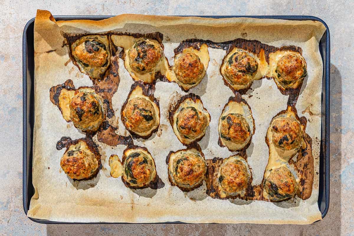 Several baked turkey meatballs spread evenly on a parchment lined sheet pan.