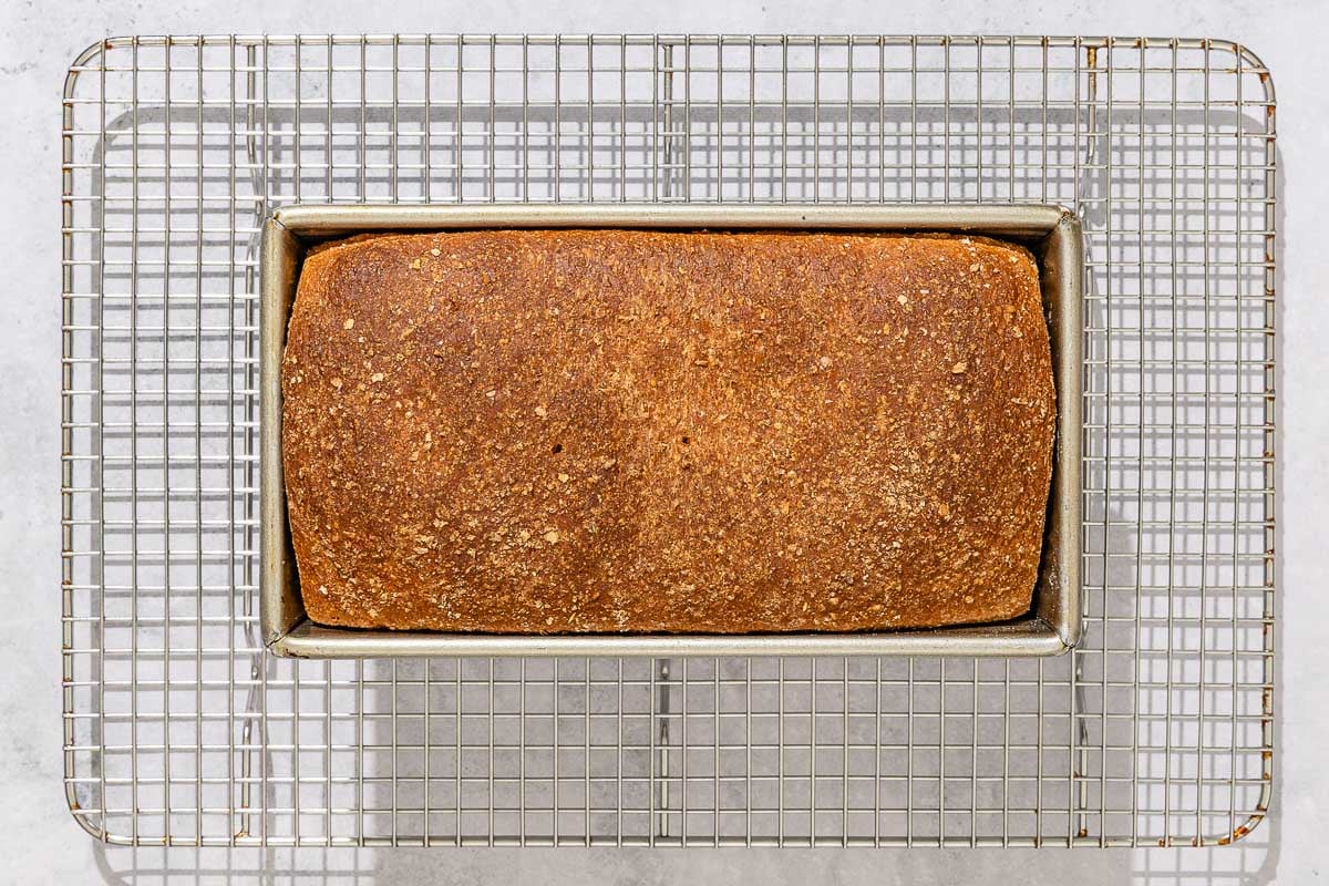 An overhead photo of a whole wheat bread loaf cooling on a wire rack.