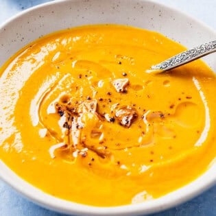 A close up of pumpkin soup topped with the Aleppo pepper-garlic oil in a bowl with a spoon.