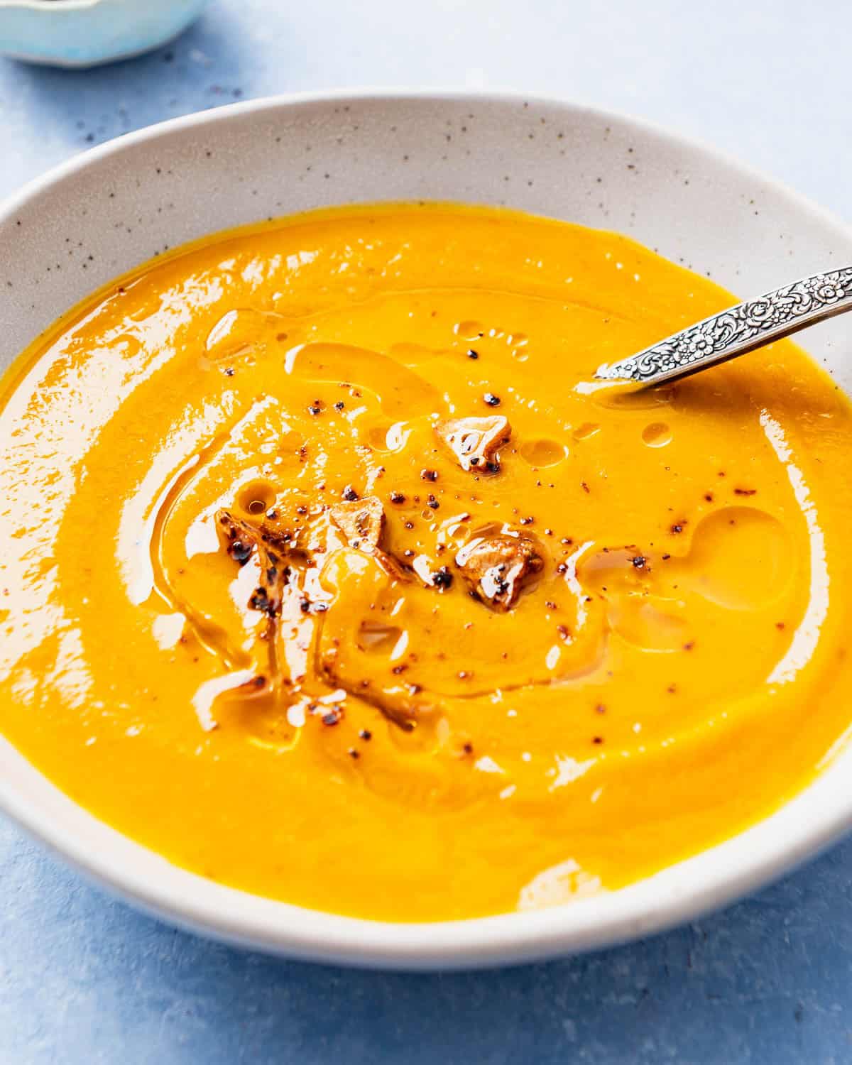 A close up of pumpkin soup topped with the Aleppo pepper-garlic oil in a bowl with a spoon.