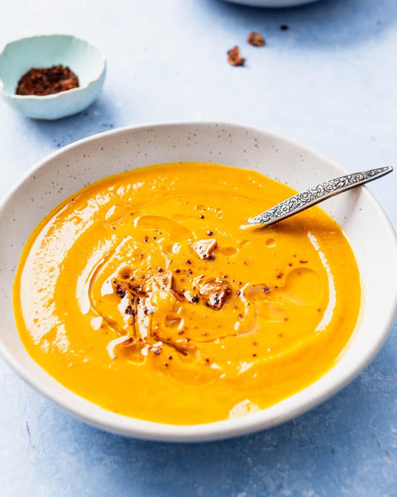 Pumpkin soup topped with the Aleppo pepper-garlic oil in a bowl with a spoon. Next to this is a bowl of Aleppo pepper.