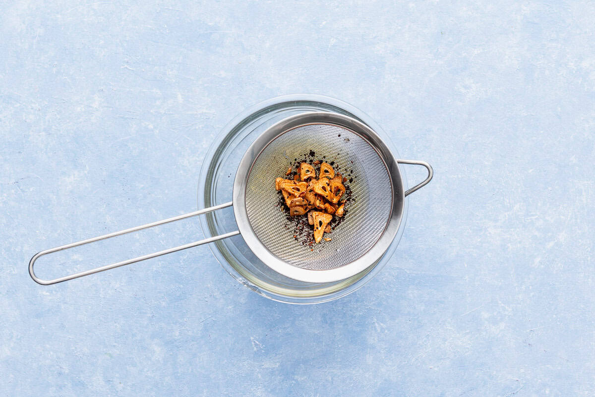 The sautéed garlic slices and aleppo pepper in a strainer sitting over a bowl of the Aleppo pepper garlic-oil.