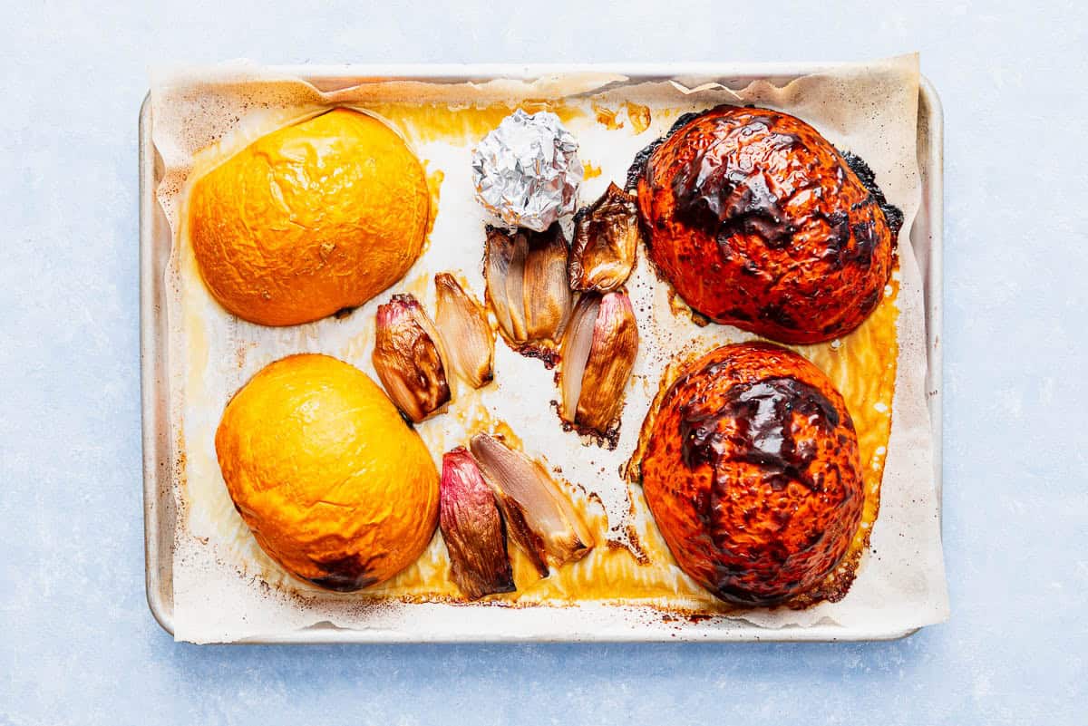 The roasted halves of kuri, shallots and garlic wrapped in foil on a parchment lined sheet pan.
