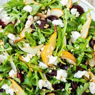 Beet and goat cheese salad on a platter next to a set of wooden serving utensils.