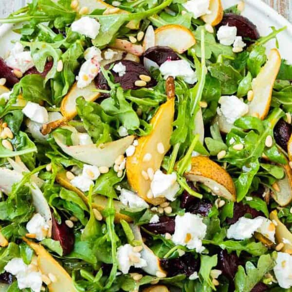 Beet and goat cheese salad on a platter next to a set of wooden serving utensils.