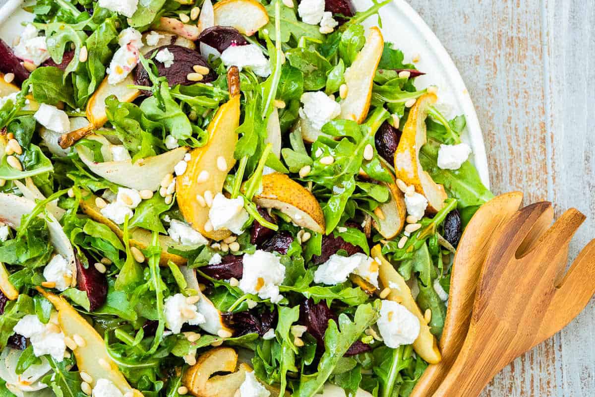 Beet and goat cheese salad on a platter next to a set of wooden serving utensils.