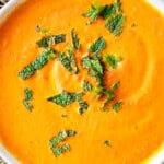 Roasted carrot soup topped with fresh mint leaves in a bowl.