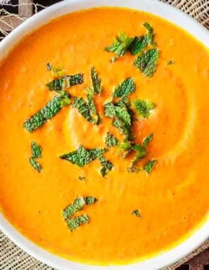 Roasted carrot soup topped with fresh mint leaves in a bowl.