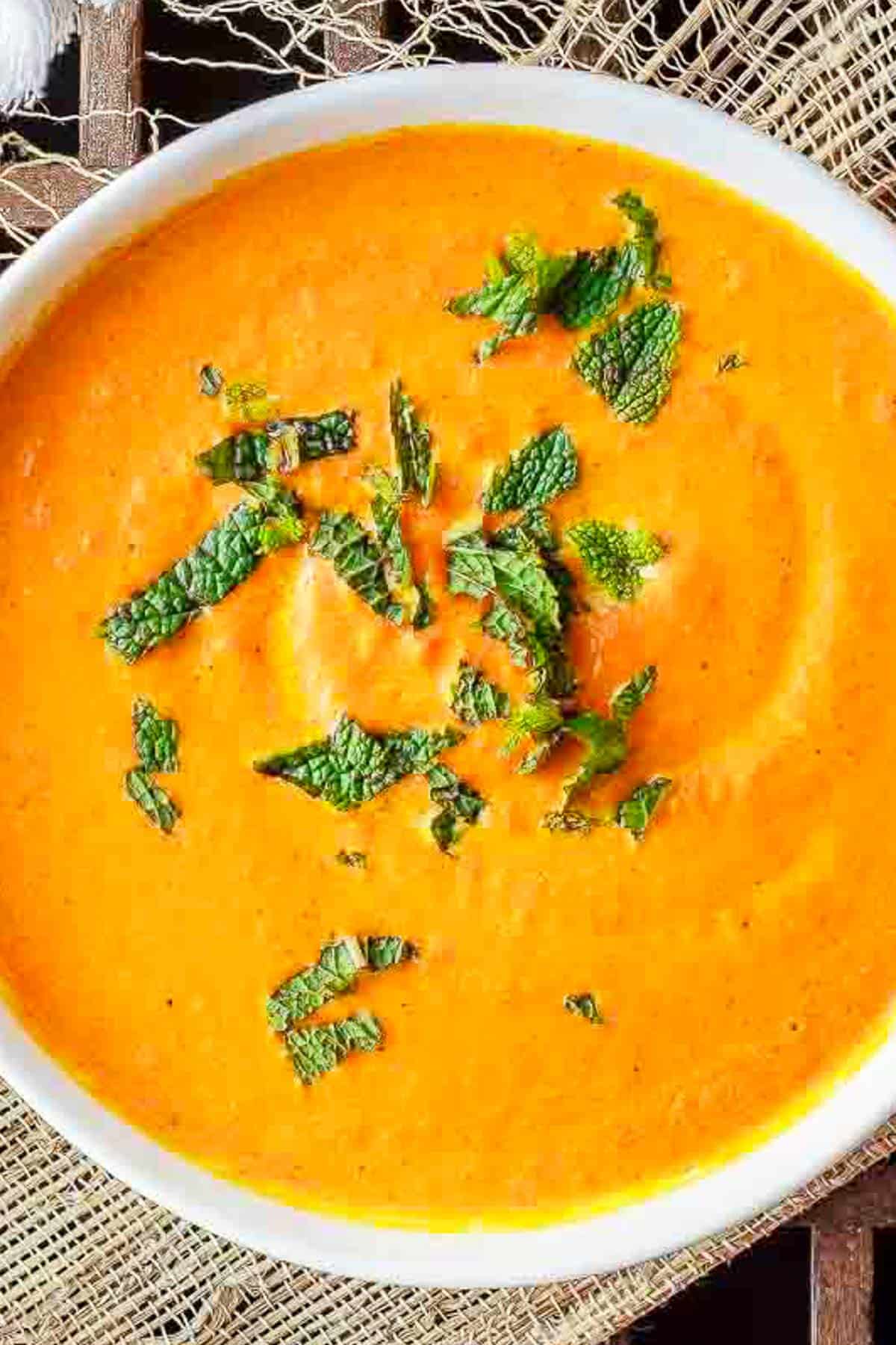 Roasted carrot soup topped with fresh mint leaves in a bowl.