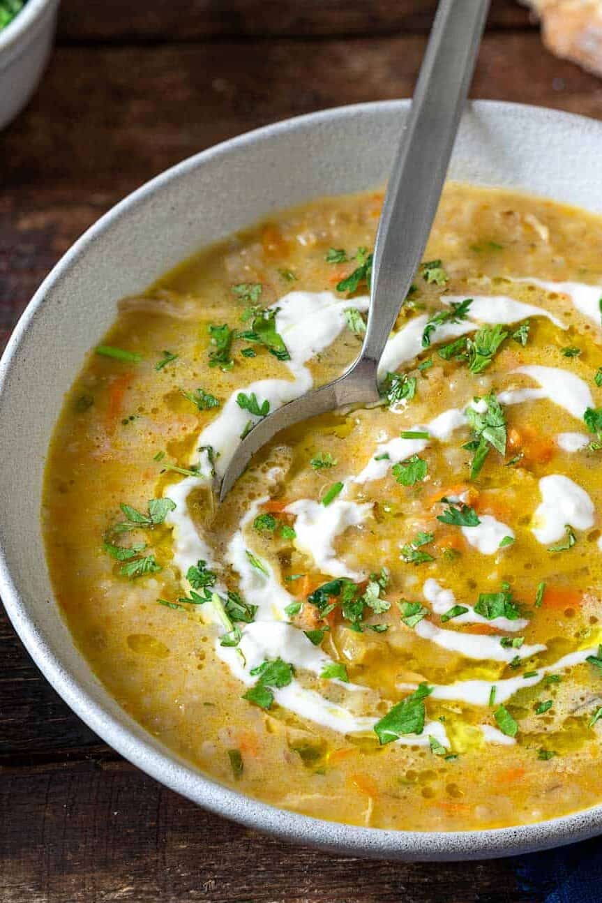 soupe jo in a bowl with a spoon garnished with half and half and chopped parsley, surrounded by small bowls of chopped parsley and half and half, and slices of crusty bread.