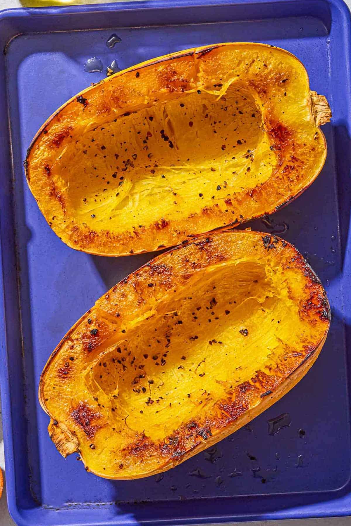 Two roasted spaghetti squash halves on a baking sheet.