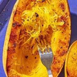 A roasted spaghetti squash half on a baking sheet being scraped with a fork.