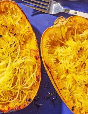 Two roasted spaghetti squash halves on a baking sheet with a fork after their flesh has been scraped.