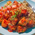 A serving of the air fryer salmon bites topped with chopped chives on a plate with quinoa, tomato cucumber salad and a fork.