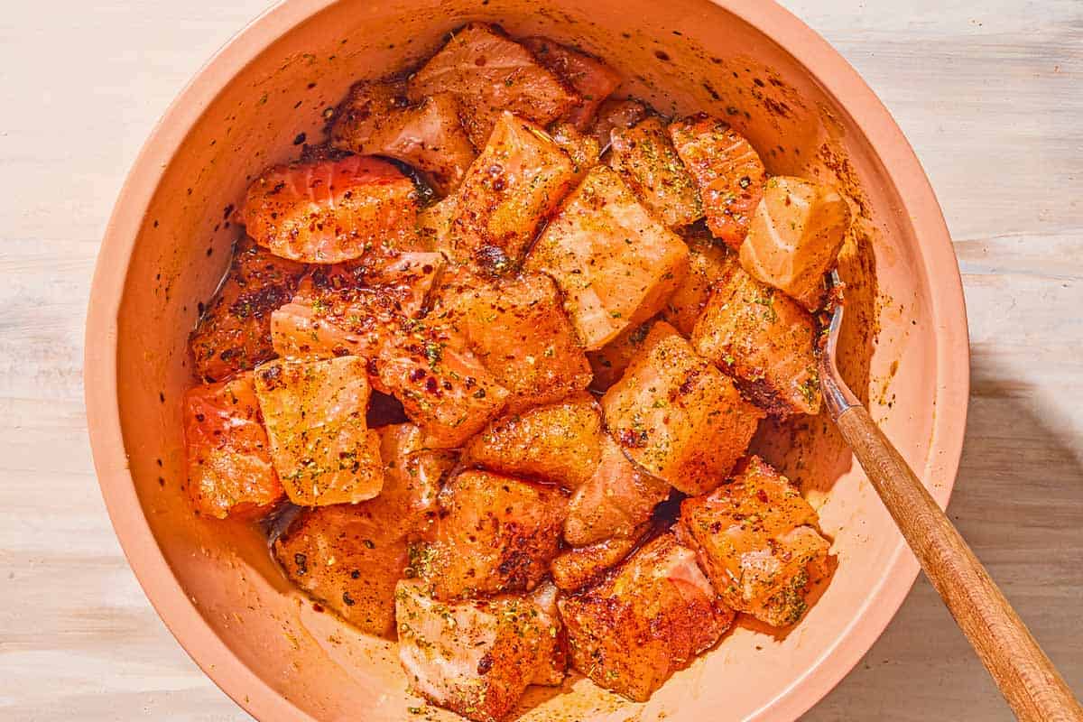 Uncooked seasoned salmon bites in a bowl with a fork.