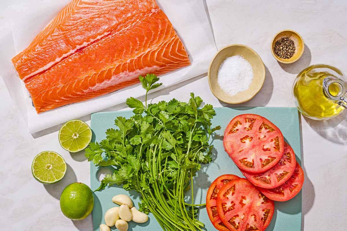 Ingredients for cliantro lime salmon including salmon, salt, pepper, tomato, lime, garlic, cilantro, and olive oil.