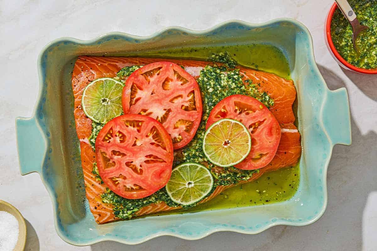 Uncooked cilantro lime salmon in a baking dish. Next to this are bowls of salt and the garlic cilantro sauce.